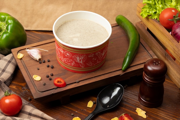 Cream mushroom soup in disposable cup bowl served with green vegetables   