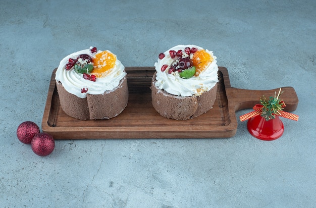 Cream topped cakes and christmas baubles on marble.