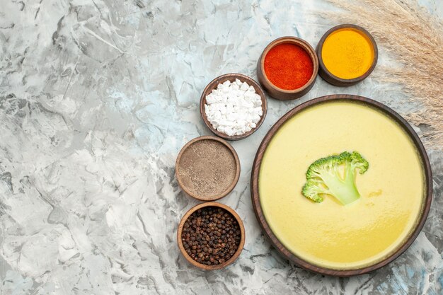 Creamy broccoli soup in a brown bowl and different spices on gray table