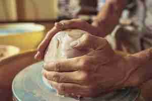 Free photo creating a jar or vase of white clay close-up. master crock. man hands making clay jug macro. the sculptor in the workshop makes a jug out of earthenware closeup. twisted potter's wheel.