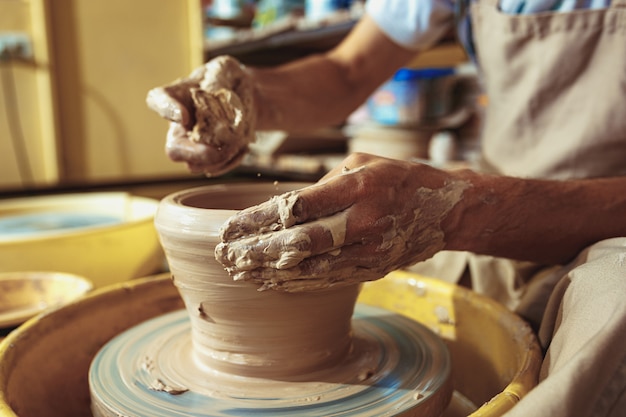 Free photo creating a jar or vase of white clay close-up. master crock. man hands making clay jug macro.