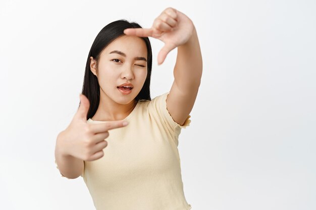 손 프레임을 통해 사진을 찍고 흰색 배경 위에 창의적으로 서 있는 순간을 측정하기 위해 창의적인 아시아 소녀