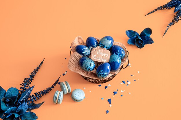 Creative Easter layout made of colorful eggs and flowers on blue.