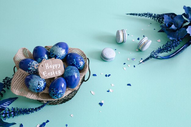 Creative Easter layout made of colorful eggs and flowers on blue.