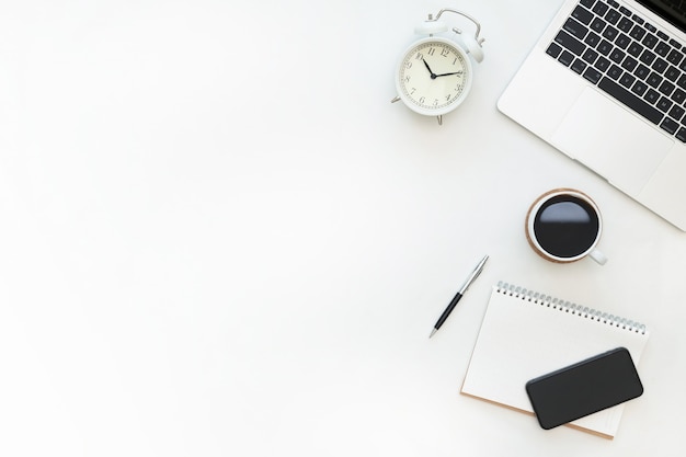 Creative flat lay design of workspace desk with laptop, alarm clock, blank notebook, smartphone and stationery with copy space background