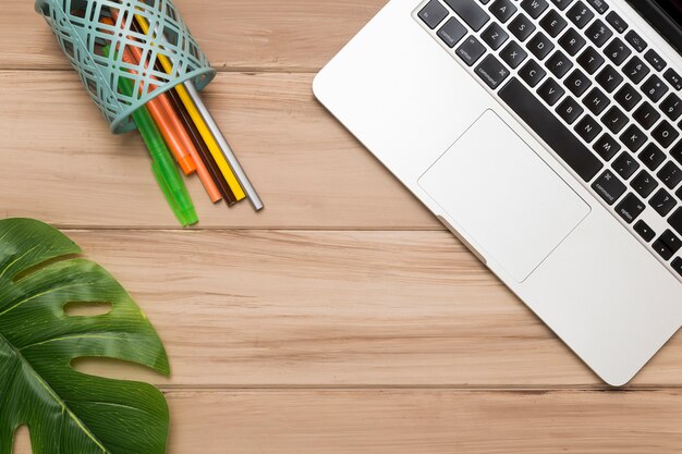 Creative flat lay of workplace wooden desk with laptop and colored pens 