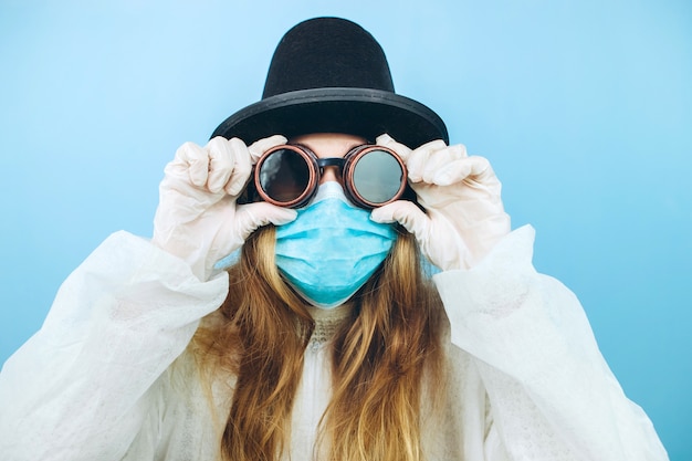 白い​ローブ​、​医療​マスク​、​メガネ​、​青い​背景​の​帽子​で​創造的​な​女の子​。​コロナ​ウイルス​隔離中​の​自己​分離​。​流行性​covid​-​2019​。