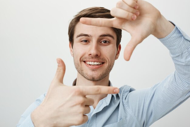 Creative handsome man smiling, showing hand frames, capture moment