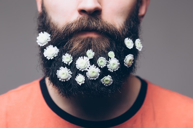 Ritratto creativo di giovane uomo bello con la barba decorata con fiori.