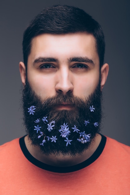 Creative Portrait of young beautiful man with a beard decorated with flowers.