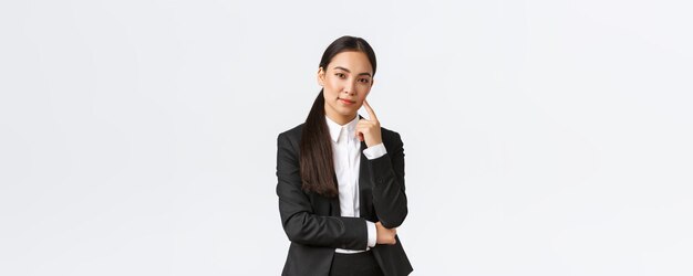 Креативная умная азиатская женщина-менеджер-продавщица в костюме, хитро улыбающаяся и смотрящая в камеру, имеет план мышления, получила отличную идею, стоящую довольная на белом фоне