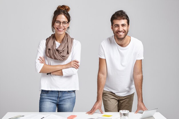 Creative team of two happy male and female colleagues in casual clothes standing at desk,