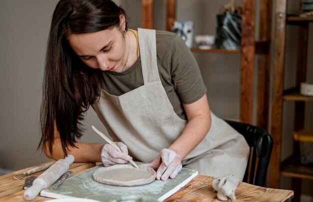 Творческая женщина делает глиняный горшок в своей мастерской