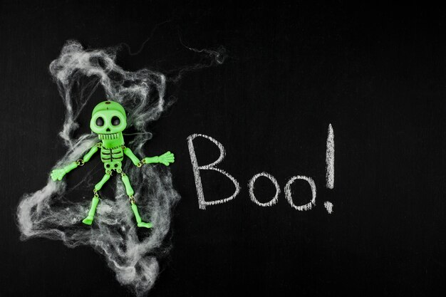 Creepy green skeleton on chalkboard with artificial web