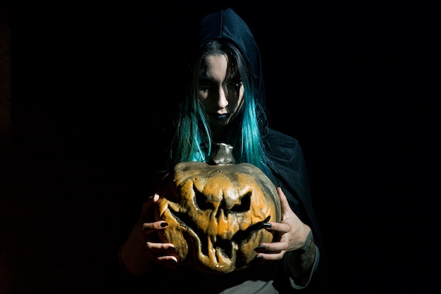 Creepy woman in hood holding pumpkin