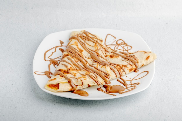 Crepe with chocolate cocoa syrup in a white plate in a white background.