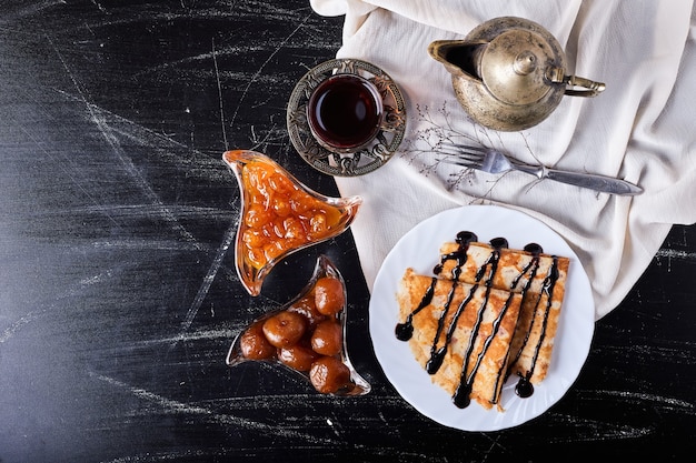 Crepes in a white plate with chocolate syrup and tea.