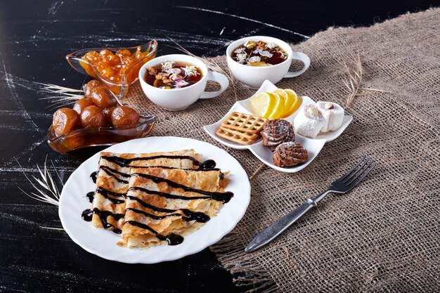 Crepes in a white plate with chocolate syrup and tea.