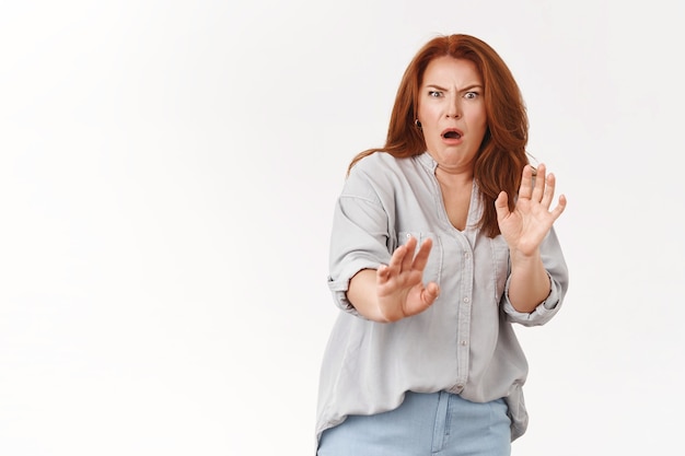 Cringing displeased redhead middle-aged woman show aversion step back reluctant raise hands defensive grimacing displeased awful terrible smell, white wall