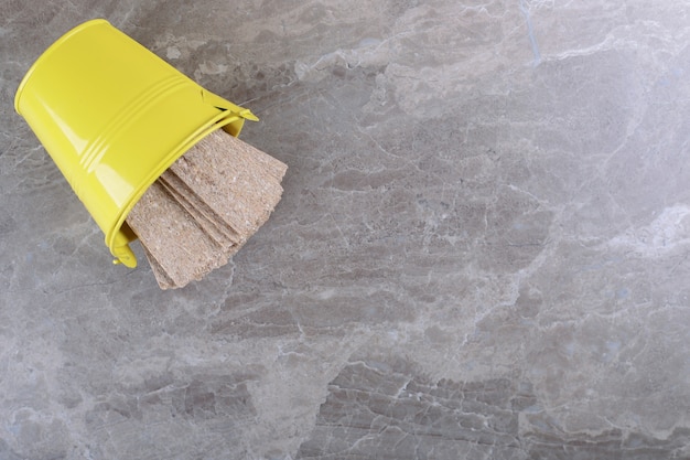 Crispbread falling from overturned yellow bucket, on the marble surface