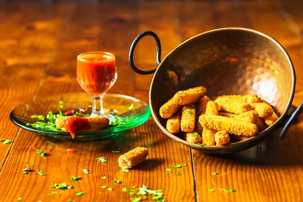 Crispy chicken fingers in copper utensil with sauce on wooden table