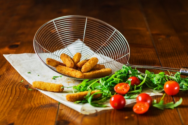 Crispy chicken fingers in skimmer with cherry tomatoes and leafy vegetable on table