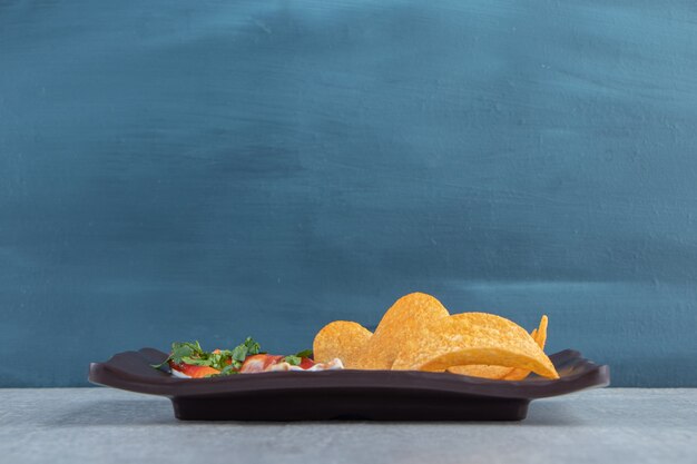 Crispy chips together with ketchup and mayonnaise on dark plate.