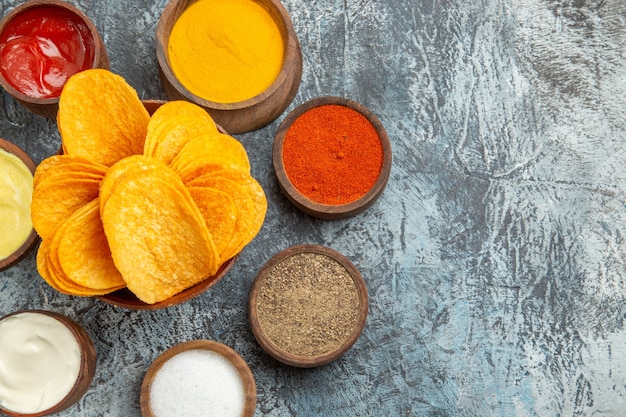 Crispy chips on wooden cutting board served with different spices mayonnaise and ketchup on gray table