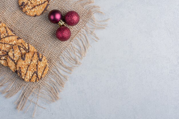 Хрустящее печенье и рождественские шары на куске ткани на мраморной поверхности