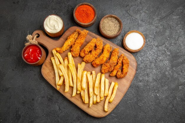 Crispy and fried chicken meal on wooden cutting board served with differen spices on dark table