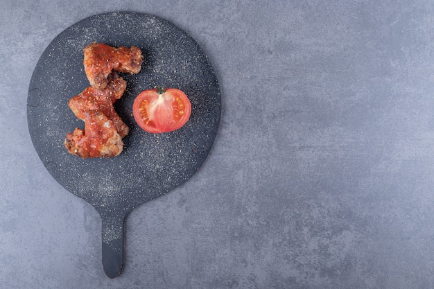 Free photo crispy fried wings and tomato on black board.