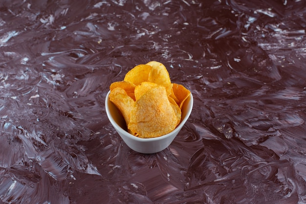 Crispy potato chips in a bowl, on the marble table. 