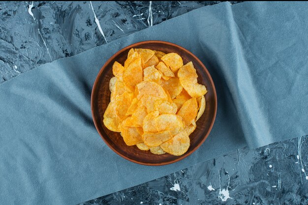 Crispy potato chips in plate on pieces of fabric , on the marble table. 