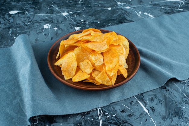 Crispy potato chips in plate on pieces of fabric , on the marble table. 