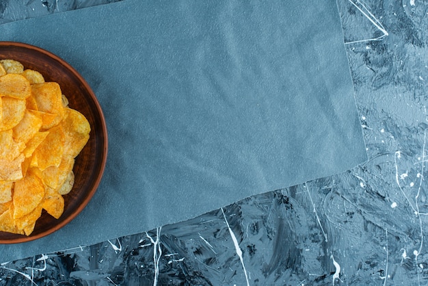 Crispy potato chips in plate on pieces of fabric , on the marble table. 