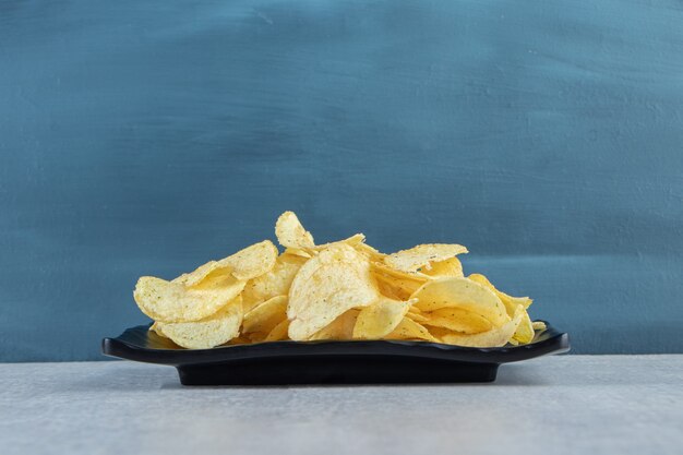 Crispy rippled chips on black plate and striped tablecloth.