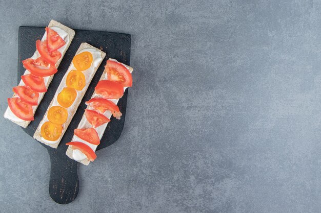 Crispy toasts with tomatoes on wooden board .