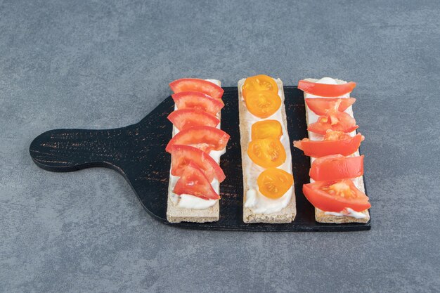 Crispy toasts with tomatoes on wooden board .