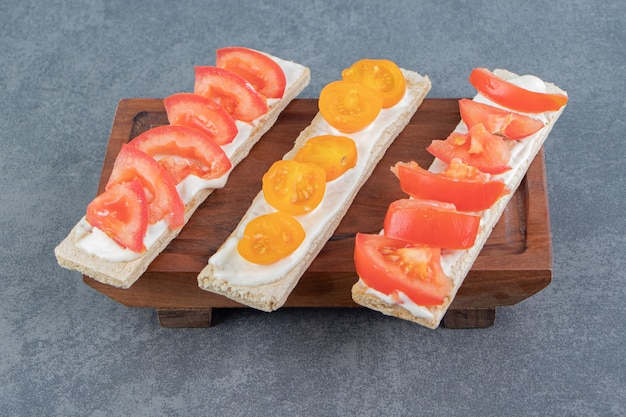 Crispy toasts with tomatoes on wooden board .