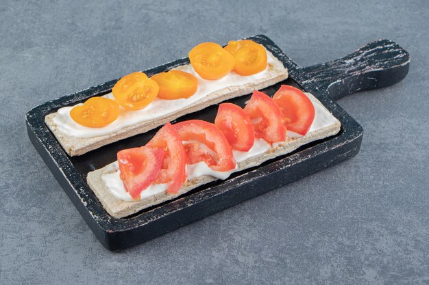 Crispy toasts with tomatoes on wooden board .