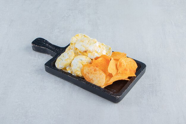 Crispy wholegrain rice cakes and chips on black cutting board.