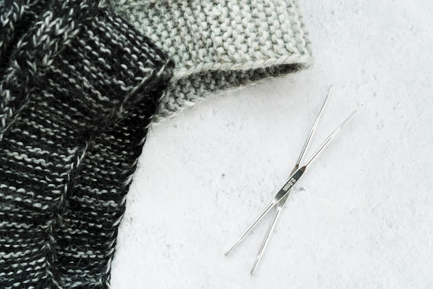 Crochet needles and knitwear fabric on white textured backdrop