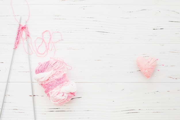 Crochet and yarn near sewing pins in pink heart shape cushion