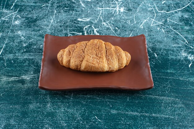 Croissant on a brown plate , on the blue background. High quality photo