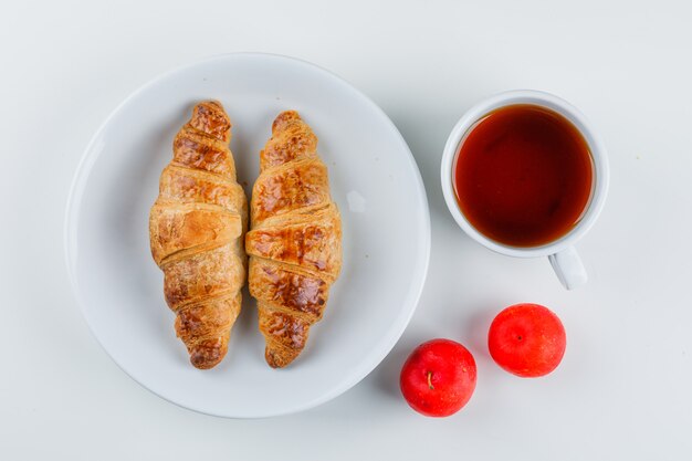 Croissant in a plate with plums, tea flat lay