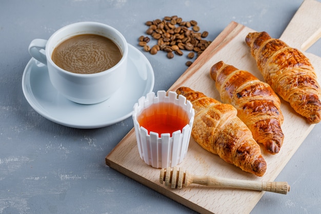 Croissant with coffee and beans, honey, dipper high angle view on plaster and cutting board