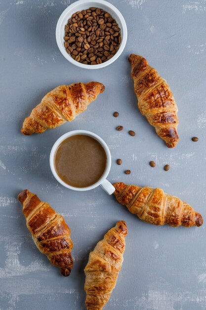 Croissant with cup of coffee, coffee beans, top view.
