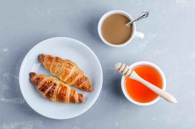 Cornetto con tazza di caffè, miele, mestolo in un piatto, piatto disteso.