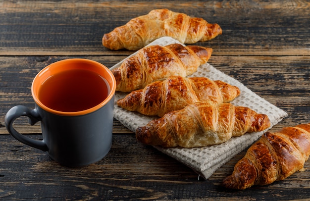 Croissant with cup of tea high angle view on wooden and kitchen towel