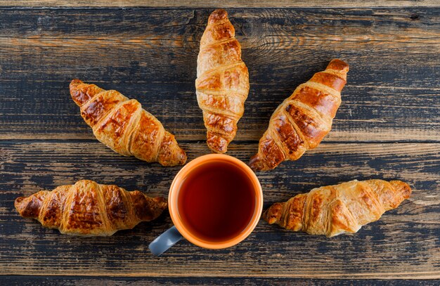 Croissant with cup of tea on wooden table, flat lay.